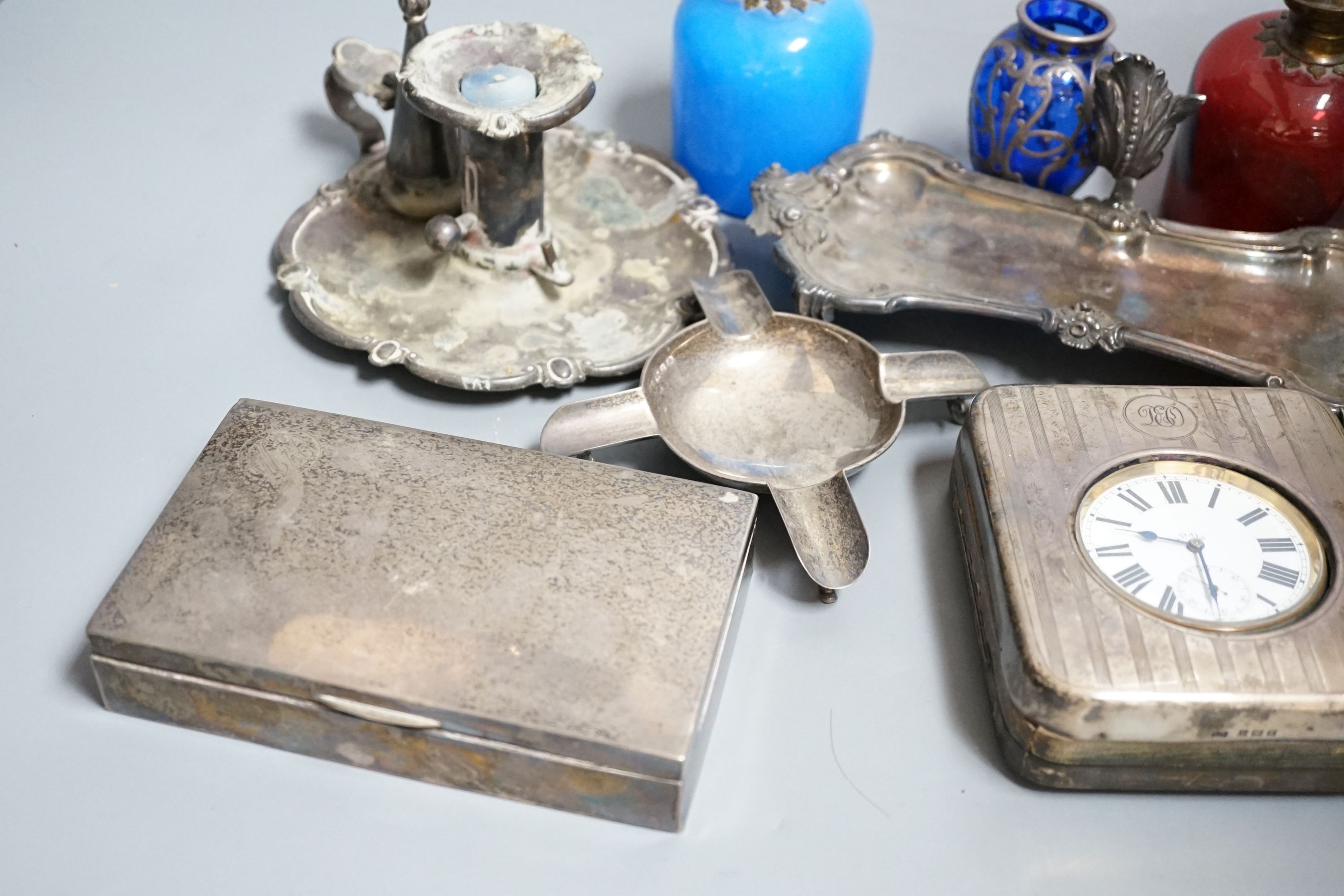 An Edwardian silver mounted travelling pocket watch case with 8-day pocket watch, one other travelling pocket watch in case, a silver mounted cigarette box, a silver ashtray, a plated snuffers stand and plated chambersti